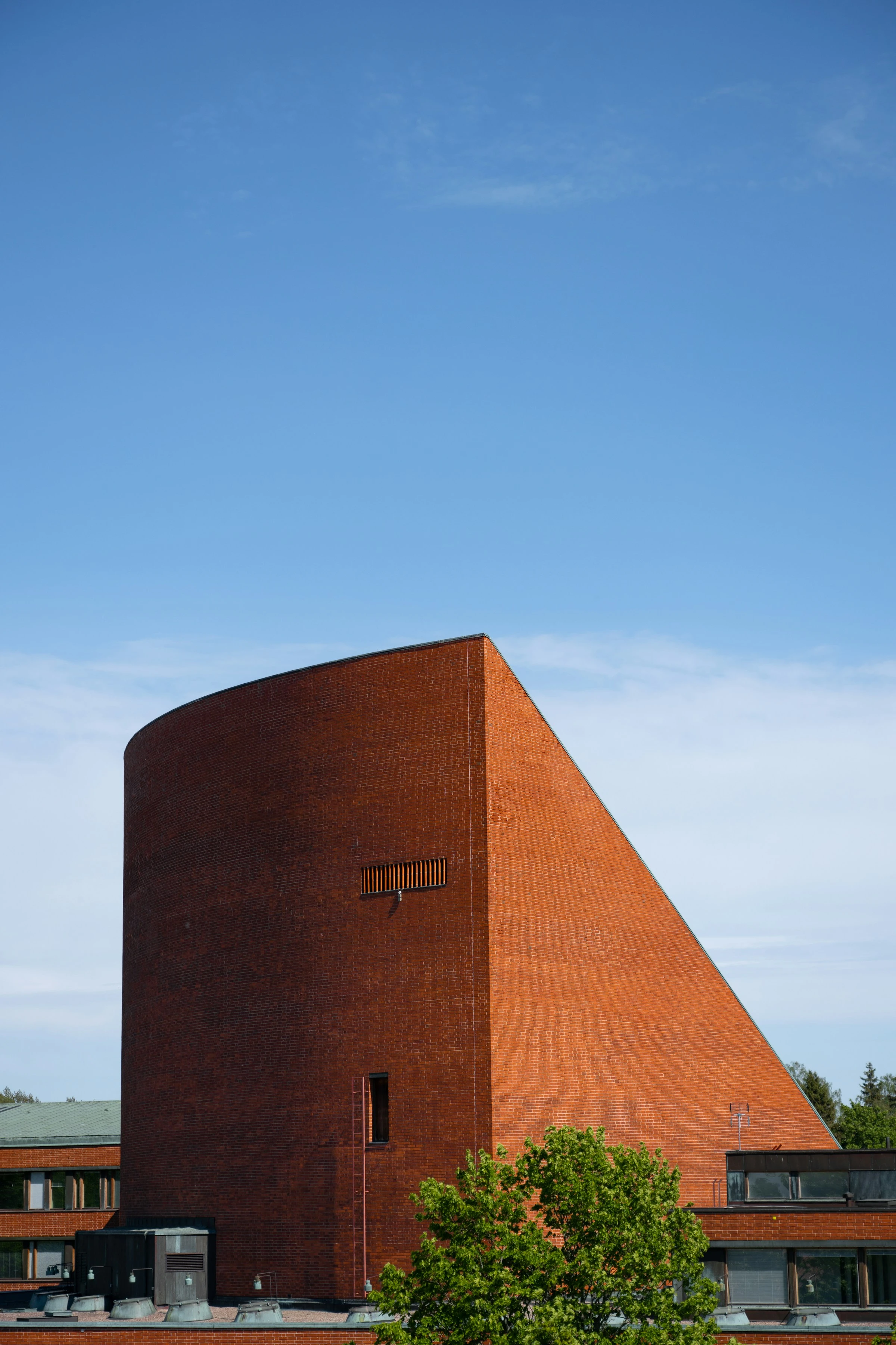 The curved red-brick auditorium of Aalto University against a clear blue sky